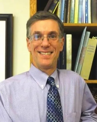 A smiling man in a business casual shirt in front of a bookshelf.