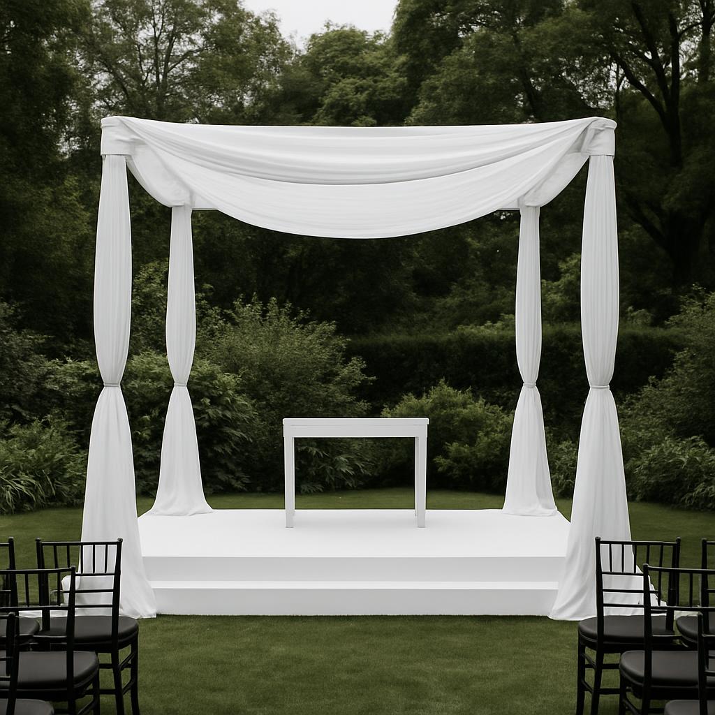 A photo of a white stage set up for an outdoor wedding, with a white table in the center and chairs on both sides.